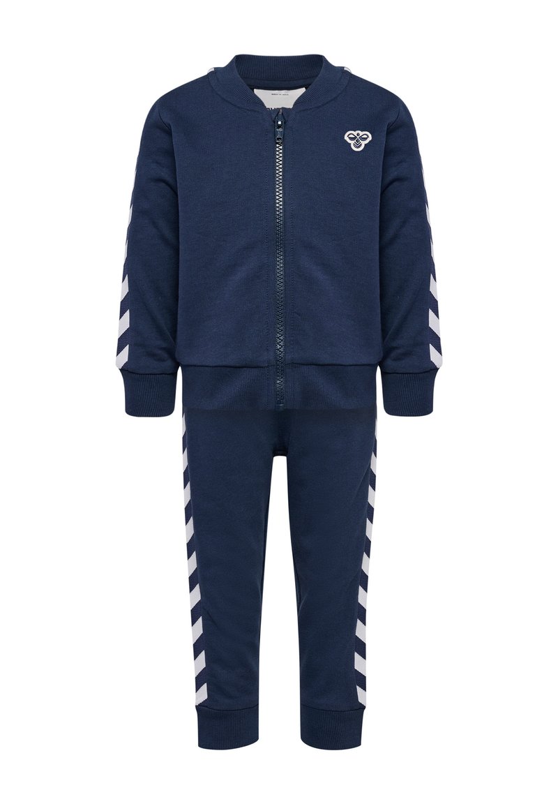 Marinblå zip-up träningsoverall med rund krage, med vita chevronränder längs ärmarna och byxorna. Tillverkad av texturerat tyg.