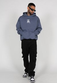 Blue hooded sweatshirt with a white graphic on the chest, paired with black cargo pants and black and white sneakers. Smooth fabric texture.