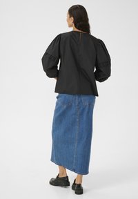 Černá blůza s nabíranými rukávy a volánkovými detaily, zkombinovaná s dlouhou modrou džínovou sukní a černými masivními botami. Minimalistický design.