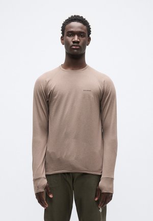 Dugih rukava, svijetlosmeđi top s teksturiranim uzorkom, okruglim izrezom i otvorima za palčeve; upareno s tamnozelenim hlačama. Logo na prsima.