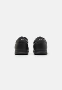 Black athletic shoes with a smooth synthetic upper, padded collar, and textured rubber sole, featuring subtle branding on the heel.