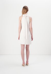 Halterneka kleita maigos beigu tonī, ar lielu aizmugures loku un piegulošu siluetu, ar taisnu apakšmalu.