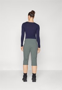 Long-sleeve navy top and knee-length green pants, made of soft fabric, with a relaxed fit and a waist belt, paired with black footwear.