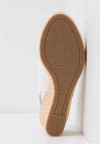 Semelle d'une chaussure compensée beige avec une semelle en caoutchouc texturée présentant un motif tressé et le marquage "Tommy Hilfiger" le long du bord.