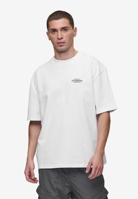 White cotton t-shirt with short sleeves, features a small black graphic design on the chest and a relaxed fit, complementing grey shorts.