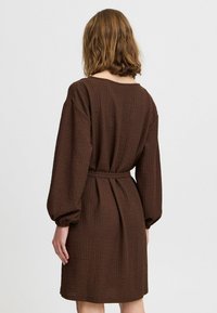 Robe marron texturée avec de longues manches bouffantes, une taille cintrée et une coupe décontractée. Le tissu présente un motif subtil et un col rond.