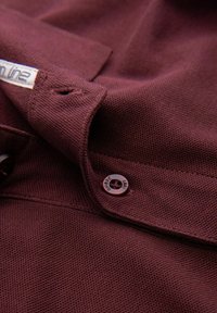 Bordová košile s texturovanou tkaninou, s špičatým límcem a knoflíkovým detailem. Etiketa viditelná na límci.