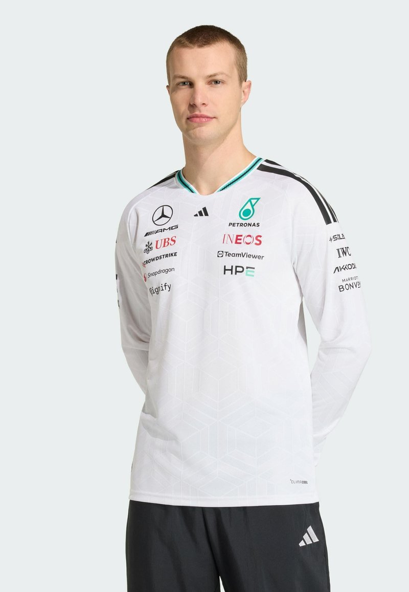 Maillot blanc à manches longues avec un motif géométrique subtil, des accents verts, des bandes noires sur les manches, logos incluant Mercedes, Petronas et Adidas.