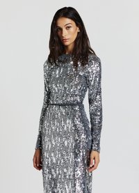 Sequined dress in silver with long sleeves, a fitted waist, and a round neckline. The fabric features a shimmering texture and patterned sequins.
