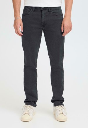 Schwarze Denim-Jeans mit schmaler Passform, ausgestattet mit fünf Taschen, dezenten Nahtdetails und einem normalen Bund. Kombiniert mit weißen Turnschuhen.