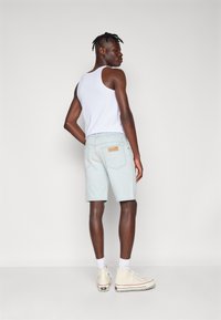 Shorts de mezclilla azul claro con un diseño ajustado, bolsillos traseros y una etiqueta de cuero marrón. Combinados con una camiseta sin mangas blanca y zapatillas altas blancas.