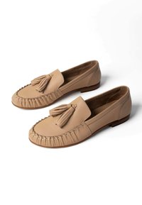 Beige leather moccasin loafers with tassels on top, stitched rounded toes, and low wooden heels, displayed on white background.