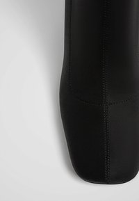 Crne gležnjače s glatkom, mat površinom. Imaju kvadratni vrh i minimalno šivanje. Elegantan dizajn bez vidljivih hardverskih elemenata ili ukrasnih detalja.
