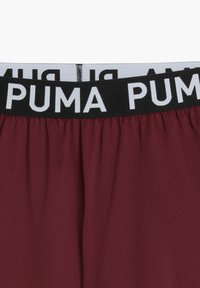 Burgundi spordilised lühikesed püksid, millel on lai must taljevöö, millel on korduv valge "PUMA" logo. Sile materjal ja elastne kujundus.