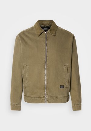 Oliven grønn zip-up jakke med kordfløyelskrage, to frontlommere og et lite rektangulært svart merke nær kanten.