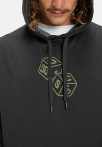 Zwarte hoodie met een trekkoord, aan de voorkant voorzien van een groene grafiek van twee dobbelstenen. Gemaakt van zacht materiaal met een ontspannen pasvorm.