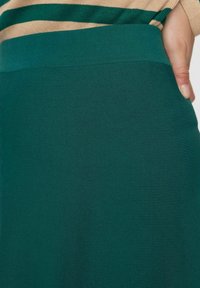 Gros plan d'une personne portant une jupe tricotée côtelée verte avec une taille haute et un haut rayé beige et vert.
