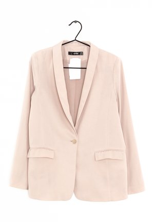 Blazer beige pour femme à un bouton, avec revers crantés et deux poches avant à rabat, suspendu sur un cintre noir avec étiquettes attachées.