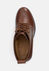 Bruine leren enkelboot met ronde neus, vetersluiting aan de voorkant, gewatteerde kraag en logo-detailing aan de binnenkant. Gladde textuur en subtiele glans.