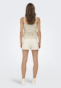 Top beige con peplum y detalles de encaje, combinado con pantalones cortos blancos. El conjunto cuenta con tirantes ajustables y un dobladillo con borde festoneado.