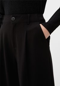 Black wide-leg trousers with a smooth texture, featuring front pockets, a single button closure, and a tailored waistband design.