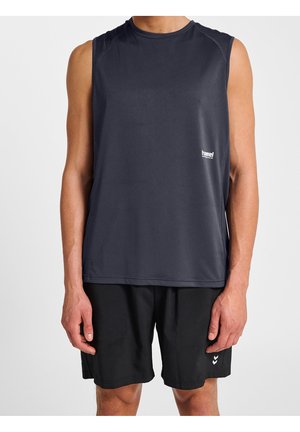 Homme portant un débardeur de sport gris foncé et un short noir, debout devant un fond blanc uni.