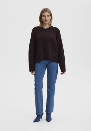 Maroon oversized sweater with soft texture, round neckline, and long sleeves, paired with blue straight-leg jeans and blue heels.