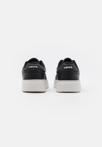 Baskets en cuir noir avec une semelle en caoutchouc blanche, dotées d'un col rembourré et d'un logo en relief à l'arrière. Lacets plats et design épuré.