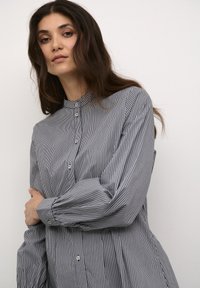 Camicia button-up a righe grigia e bianca, con colletto alto e maniche lunghe con polsini arricciati. Tessuto di cotone morbido.