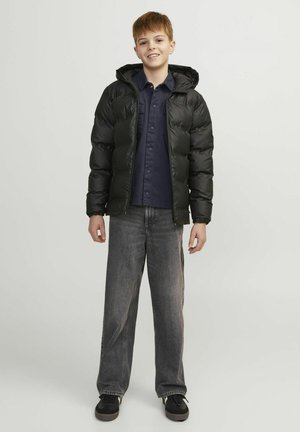 Veste matelassée noire avec capuche, fermeture éclair et poignets élastiques, associée à une chemise boutonnée marine et un jean large gris. Baskets noires.