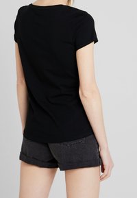 Camiseta negra de manga corta de algodón, con un cuello redondo y un ajuste holgado, combinada con pantalones cortos oscuros de corte enrollado.