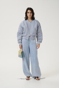 Giubbotto puffer grigio con chiusura a zip, pantaloni larghi in denim blu chiaro e borsa bicolore. Sandali neri completano l'outfit.