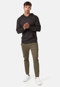 Sudadera de punto gris oscuro con mangas largas y un bolsillo frontal, combinada con pantalones tapered verdes oliva y zapatillas blancas.