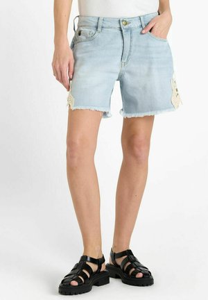 Lichte blauwe denim short met een rafelige zoom, gemaakt van een gestructureerde stof en unieke accenten aan de zijkanten. Draag het met zwarte sandalen met bandjes.