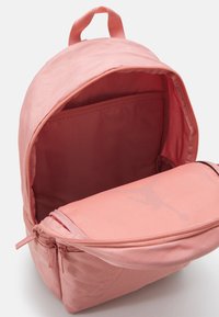 Zaino rosa realizzato in tessuto resistente, dotato di un ampio scomparto principale e una tasca con zip. L'interno ha una tessitura liscia con dettagli del marchio.