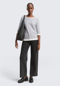 Randig stickad tröja i grått och vitt med trekvartsärmar, kombinerad med högmidjade svarta vida jeans och svarta klacklösa loafers.