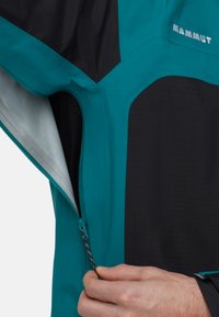 Teal en zwarte waterdichte jas met een ritssluiting zak en textuurstof. Inclusief gedetailleerde stiksels en een getailleerd ontwerp.