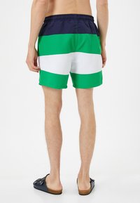 Bañadores de hombre con rayas horizontales en azul marino oscuro, verde, blanco y verde claro. Cintura elástica con un corte relajado y textura suave.