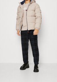 Beżowa pikowana kurtka z kapturem, granatowa podszewka, zapięcie na zamek. Jasnoszara bluza i czarne spodnie w kratę. Czarne masywne buty.