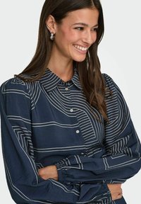 Marineblauwe blouse met witte strepen, met een knoopsluiting kraag, opgeblazen mouwen en elastische manchetten. Zachte textuur met een lichtgewicht ontwerp.