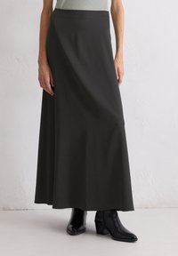 Lange schwarze Rock aus weichem, fließendem Stoff mit glatter Textur, featuring eine hohe Taille und eine leicht ausgestellte Silhouette, kombiniert mit schwarzen Stiefeln.