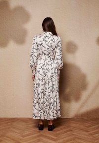 Μάξι φόρεμα με μακριά μανίκια και στρώσεις, σε εκρού βάση με μαύρα μοτίβα ψαλιδιών, μέση με ζώνη και ρέουσα σιλουέτα.