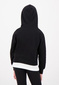 Sweatshirt à capuche noire en tissu doux avec un design court. Présente des poignets et un ourlet côtelés. Superposé sur une chemise blanche.