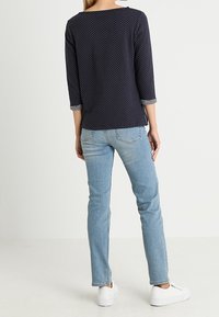 Navy polka dot top with three-quarter sleeves, paired with light denim jeans and white sneakers. Back view shows striped sleeve accents.
