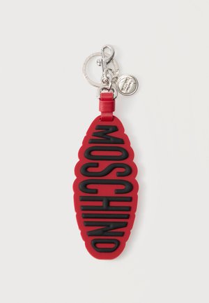 Rød oval nøglering med sort forhøjet "MOSCHINO"-tekst, sølvnøglering, hummerlås og lille rundt brandmærke fastgjort.