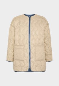 Chaqueta beige acolchada con cremallera y ribete azul marino, con dos bolsillos delanteros y patrón ondulado de costuras sobre fondo claro.