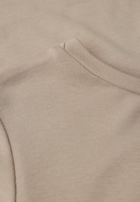 Beige stof met een gladde textuur. Ronde halslijn en korte mouwen. Detailweergave die het zachte, gelijkmatige breipatroon zonder zichtbare naden toont.