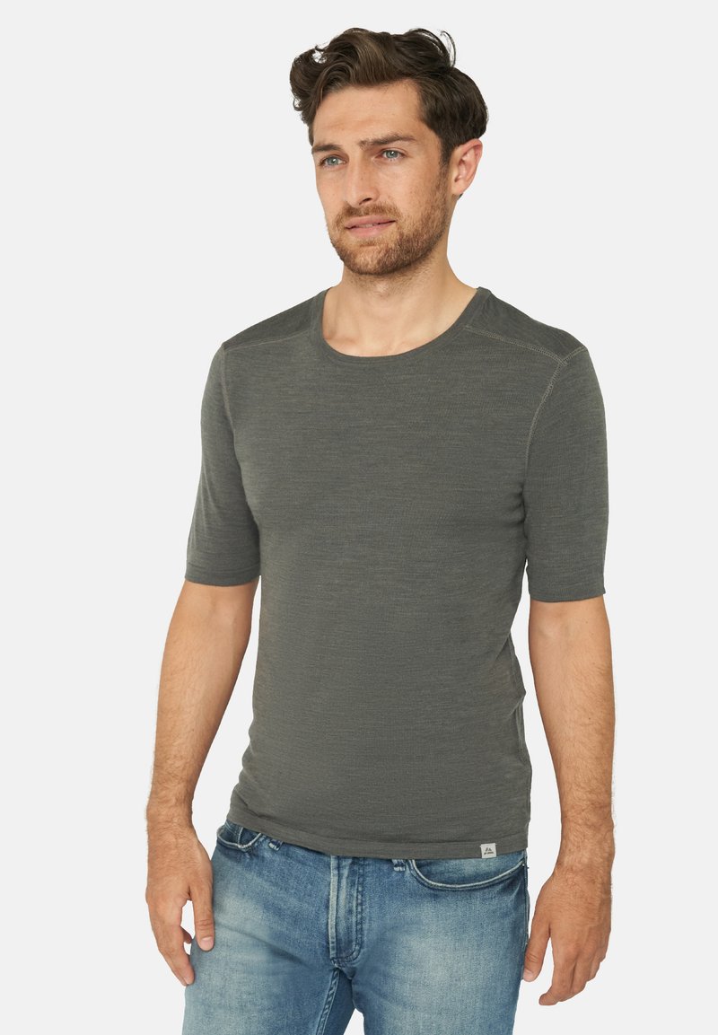 T-shirt a maniche corte con collo rotondo in tessuto verde scuro con una finitura testurizzata e dettagli di cucitura sottili, abbinato a jeans blu.
