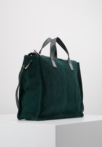 Tumma vihreä samettinen käsilaukku, jossa on nahkakahvat, suorakulmainen muoto, sileä pinta ja yksinkertainen muotoilu. Varustettu vetoketjulla ja laadukkaalla ompelulla.