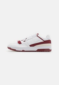Sneakers bianchi con accenti bordeaux, tomaia in pelle, collo imbottito e suola in gomma testurizzata. Presenta un logo sul lato e chiusura con lacci.